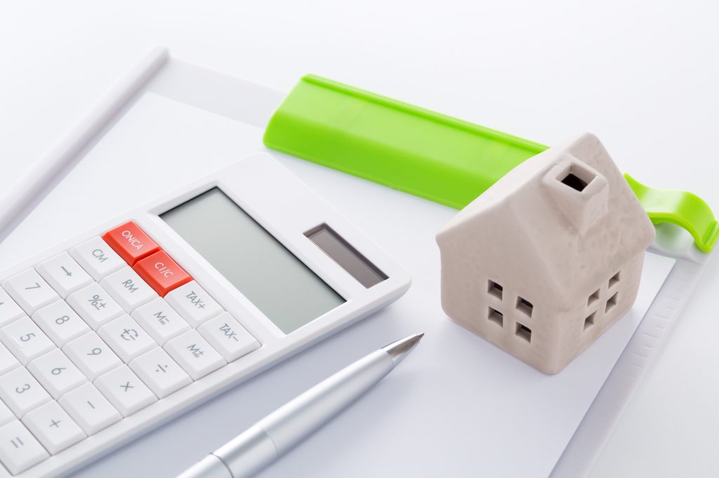 白い机に置かれた電卓と家の模型