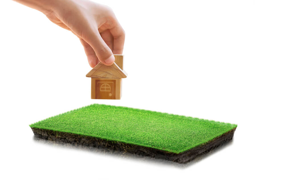 四角く切り取った芝生の上で家の模型を持つ手